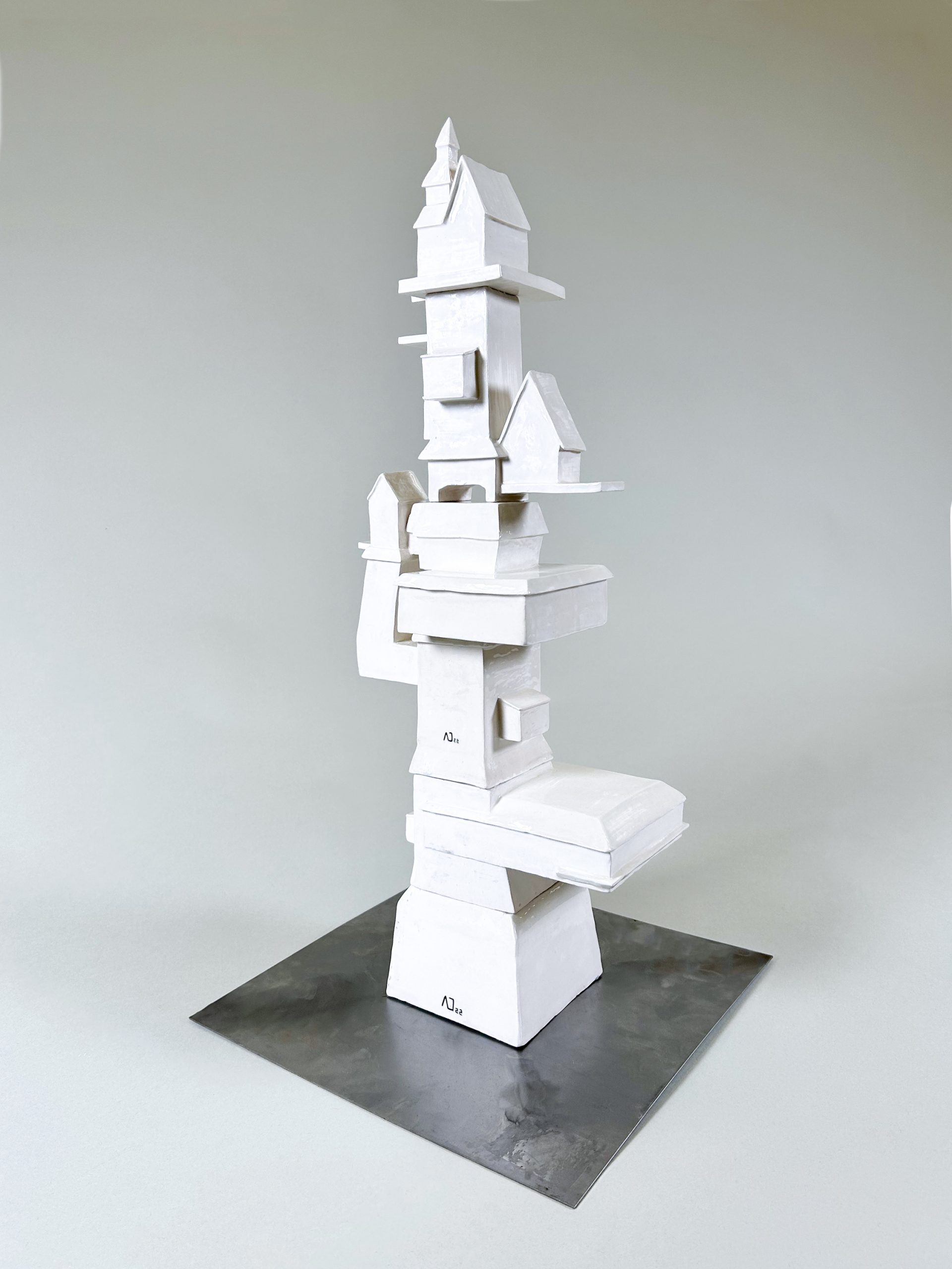 A 2-foot tall white, ceramic tower standing at a 3-quarters angle. It has a 1-foot-wide block as a foundation and becomes narrower as it approaches the top. It is topped with a house-like structure with a triangular roof. The tower has three structures that come out on the sides, attached diagonally on the opposite side of the tower. The bottom-most addition is a flat box. the middle-most is a perpendicular arm that upholds a small house-like building. Not far above is a medium-sized house-like structure on a thin base. the artist says. 